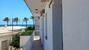 Un couloir étroit avec un mur blanc, une rambarde métallique et une vue sur la mer et les palmiers.