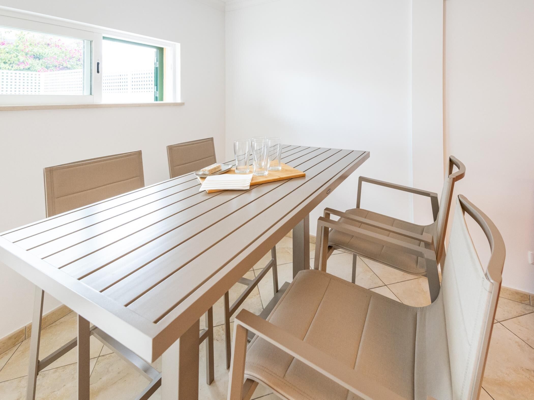 A dining area with a long wooden table, six chairs, and a window with a view of greenery.