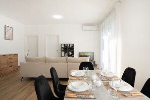 Un comedor con una mesa dispuesta para cuatro personas, un sofá y una televisión al fondo.