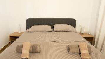 A neatly made bed with striped bedding, two pillows, and two rolled towels. There are two bedside tables with lamps and a remote control on one.