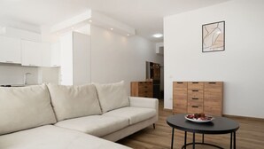 A modern living room with a beige sofa, a round black table with a bowl of fruit, and wooden cabinets. - Sea View-Expansive Apartment by TOK (Golem)