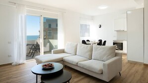 A modern living room with a white sofa, a dining table, and a kitchen area. - Sea View-Expansive Apartment by TOK (Golem)