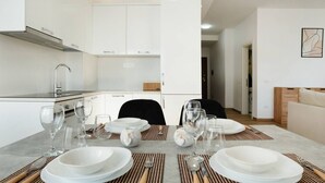 A modern kitchen with white cabinets, a built-in stove, and a dining area set with white plates, glasses, and cutlery. - Sea View-Expansive Apartment by TOK (Golem)