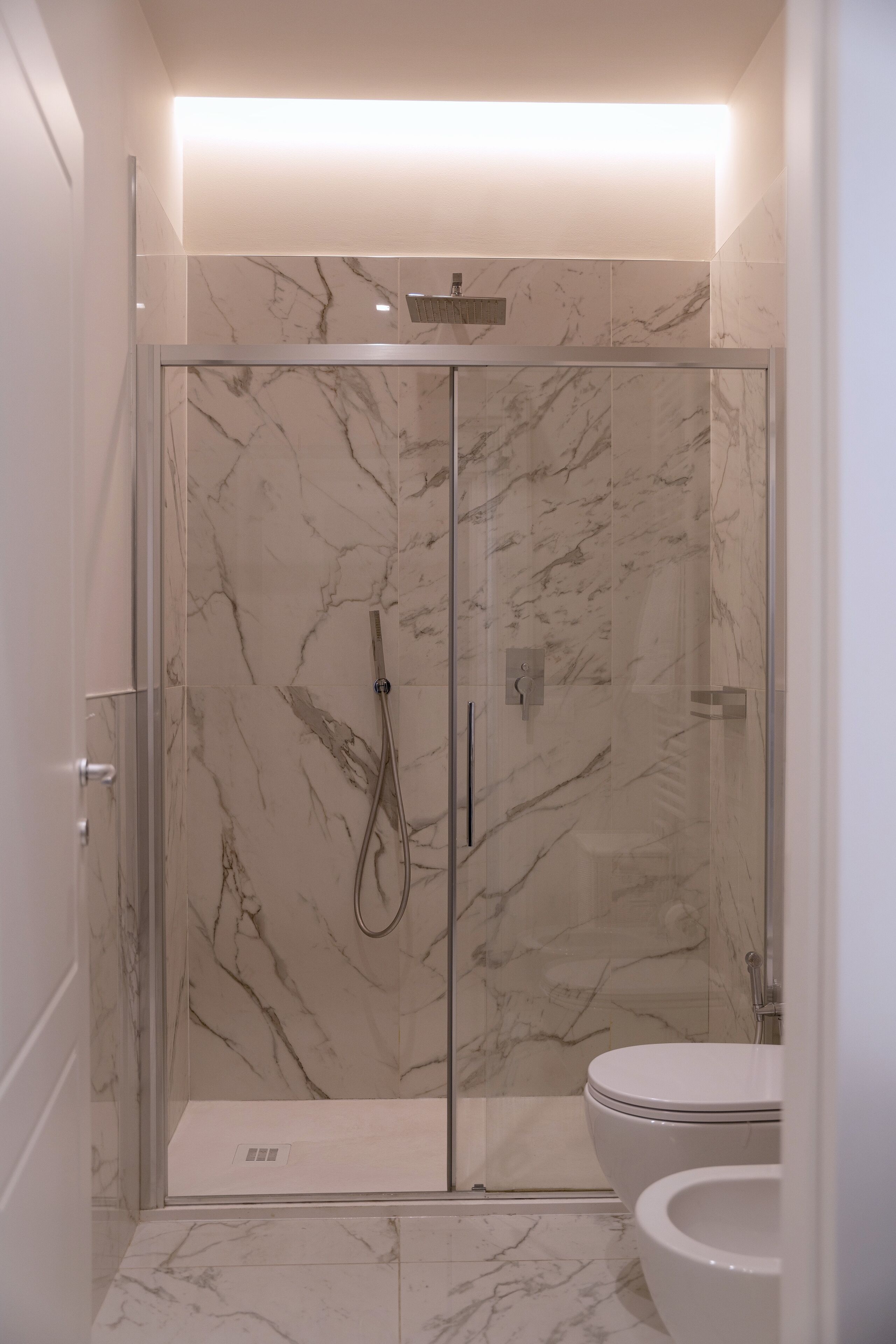 Une salle de bain moderne dotée d’une douche à parois de verre, de toilettes et d’un revêtement de sol en marbre.