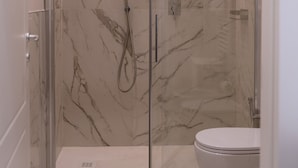 Une salle de bain moderne dotée d’une douche à parois de verre, de toilettes et d’un revêtement de sol en marbre.
