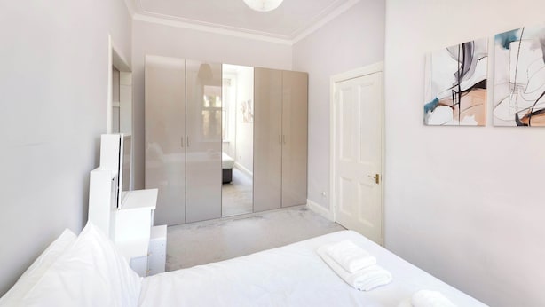 A modern bedroom with a bed, a wardrobe, and a door. - Refined 2-Bed Flat with Classic Edinburgh Charm (Edinburgh)