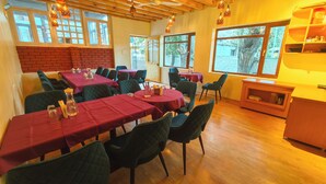 Un comedor con varias mesas cubiertas de manteles rojos, sillas verdes y faroles colgantes.