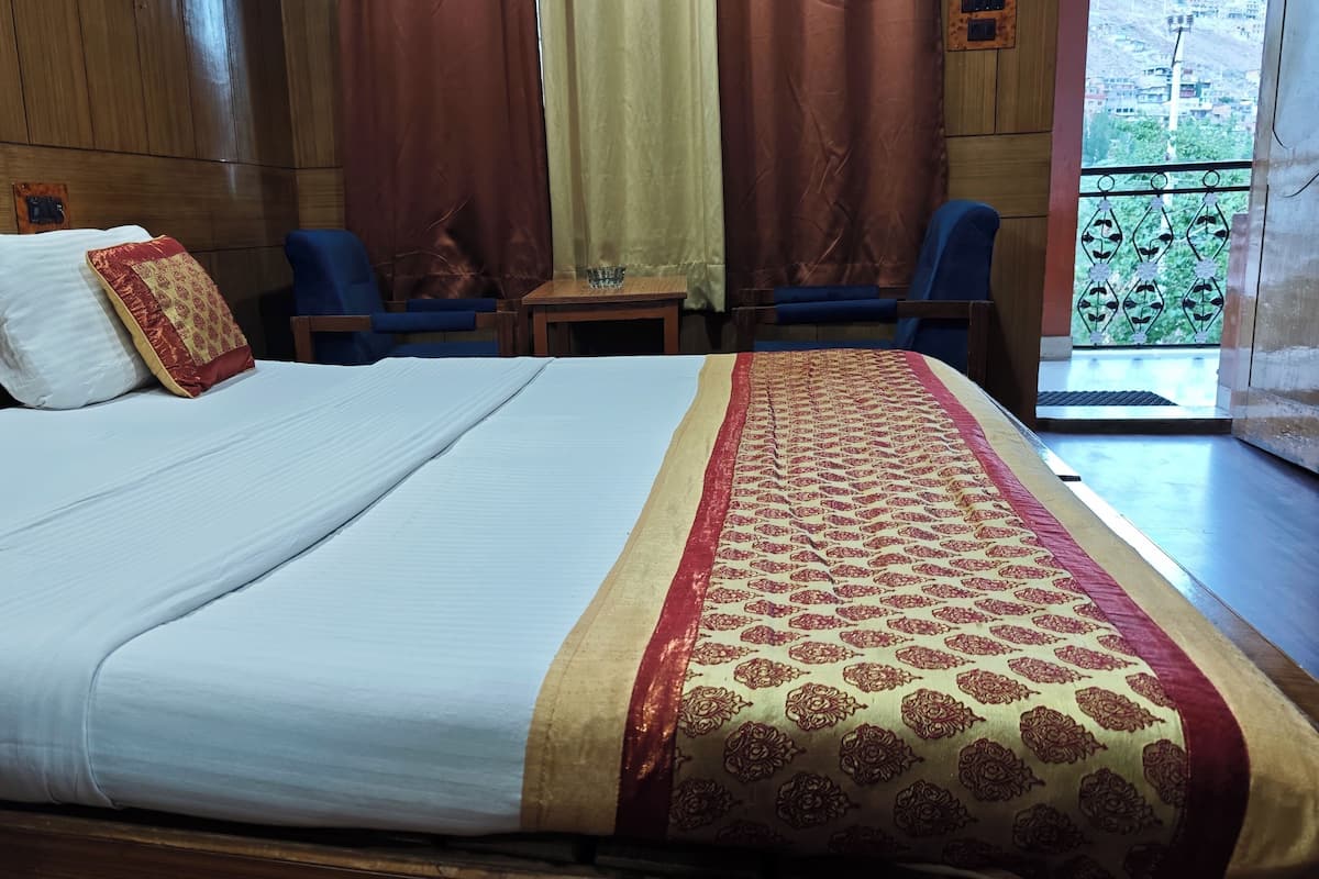 Habitación de hotel con una cama grande, dos sillas, una mesita y vistas al exterior.