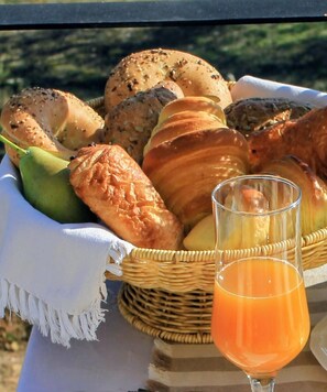 Een mand met verschillende soorten brood en een glas sinaasappelsap op een tafel.