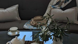 Een kamer met een bank, een tafel met theepot en kopje, en een raam met uitzicht op gebouwen.