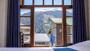 A bedroom with a large window, a bed, and a view of a mountain landscape. - Flamingo Resort (Manali)