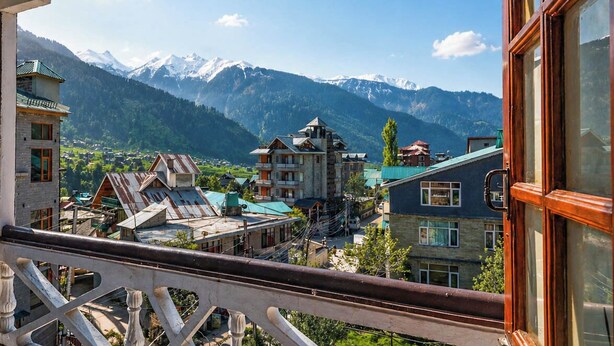 A balcony with a view of a mountain range and a village below. - Flamingo Resort (Manali)