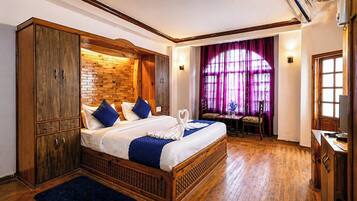 A double bed with a wooden headboard, a small table with chairs, and a window with purple curtains.