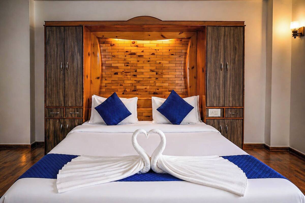 A hotel room with a large bed, wooden headboard, and a heart-shaped towel arrangement.