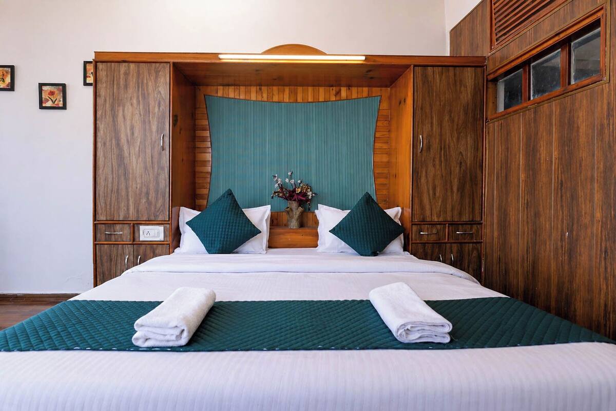 A hotel room with a large bed, wooden wardrobe, and a teal accent wall.
