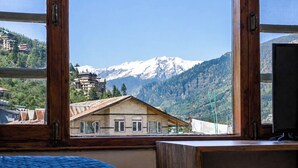 A room with a wooden desk, a bed, and a window with a mountain view. - Flamingo Resort (Manali)