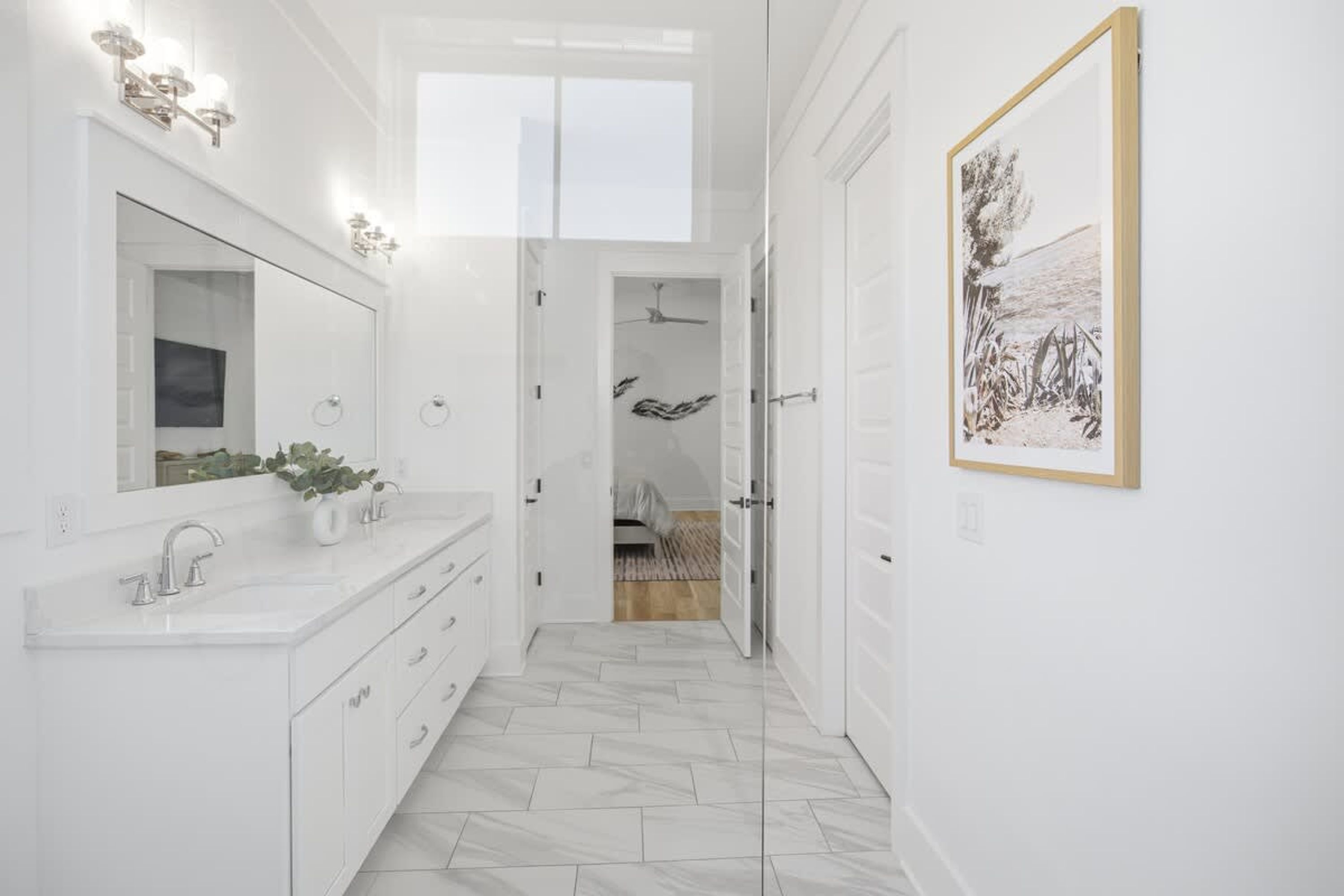 A modern bathroom with a large mirror, white vanity, and a framed artwork on the wall.