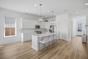 A modern kitchen with white cabinetry, a central island with bar stools, and pendant lighting. - 7BR Heart of Home W Pool Near the Beach (Miramar Beach)