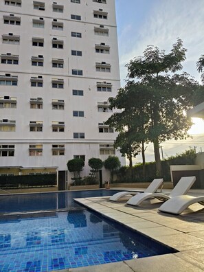 Un hôtel doté d’une piscine, de chaises longues et d’un grand arbre.