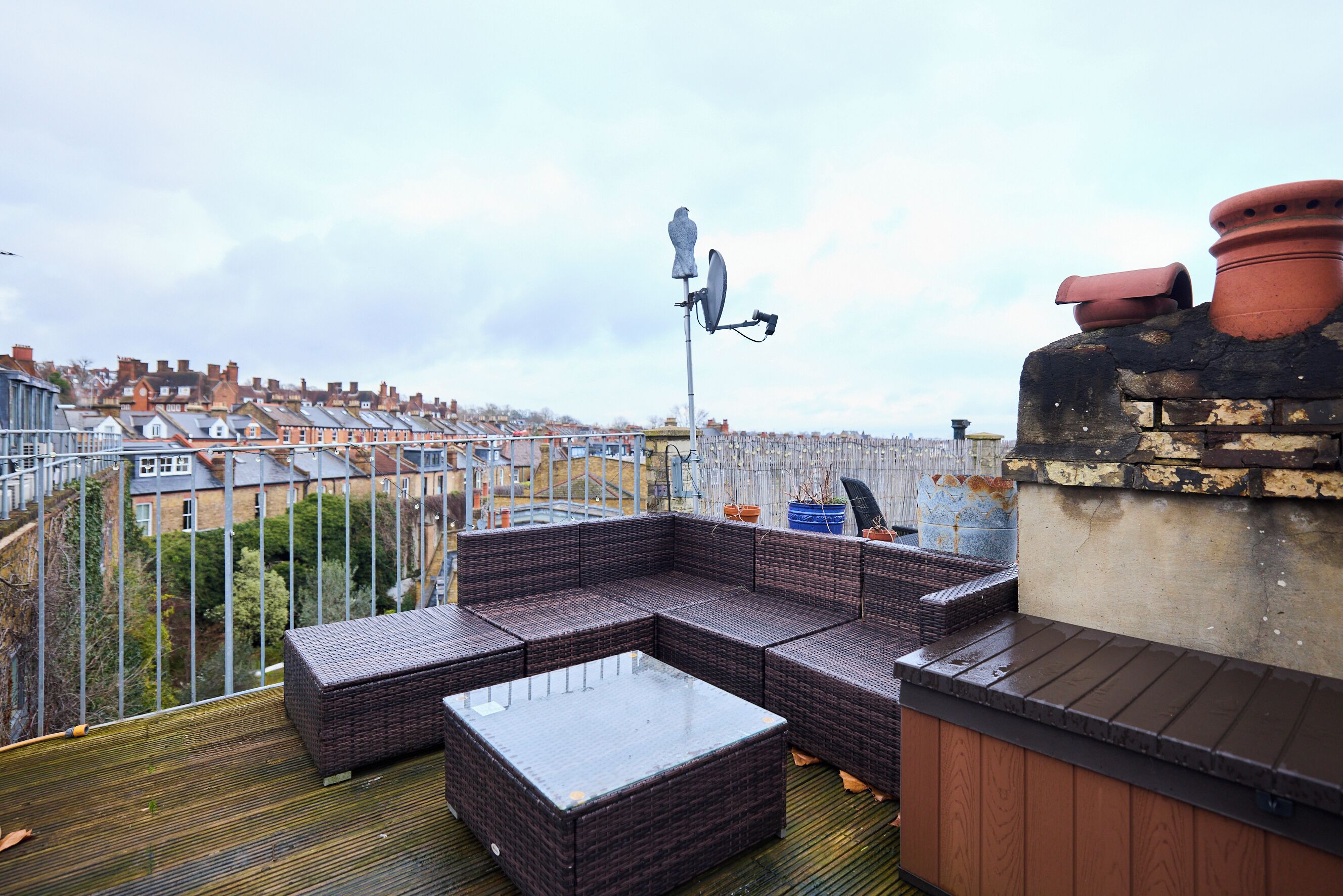 Une terrasse sur le toit, avec un ensemble de meubles de jardin en osier, une antenne parabolique et des pots en terre cuite.