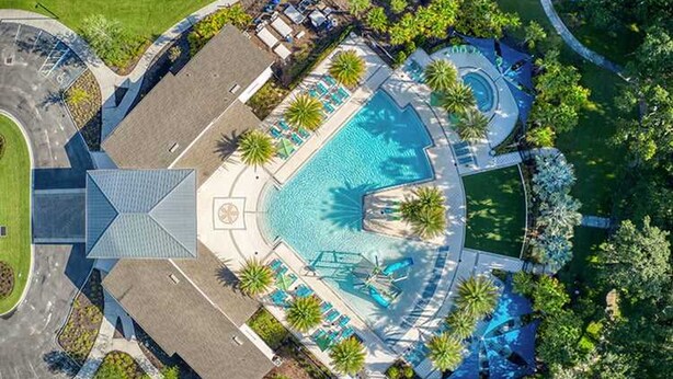 Vista aérea de un resort con piscina central, áreas de descanso y palmeras.