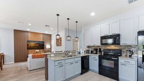 Una cocina moderna con armarios azul claro, una isla central, electrodomésticos de acero inoxidable e iluminación colgante.