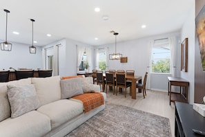 A modern living room with a sofa, dining table, and chairs. - Luxurious 5-bedroom House With Pool Near Disney World - Perfect for Your Family 2613 (Kissimmee)