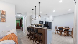 Una cocina moderna con una isla central, taburetes de bar y un comedor con sillas de madera y una mesa.
