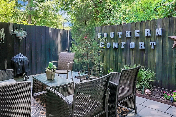 A patio area with wicker furniture, a table with a potted plant, and a wooden fence with "Southern Comfort" signage. - Charming Townhouse Retreat w/ Patio & Private Balcony Escape (North Charleston)