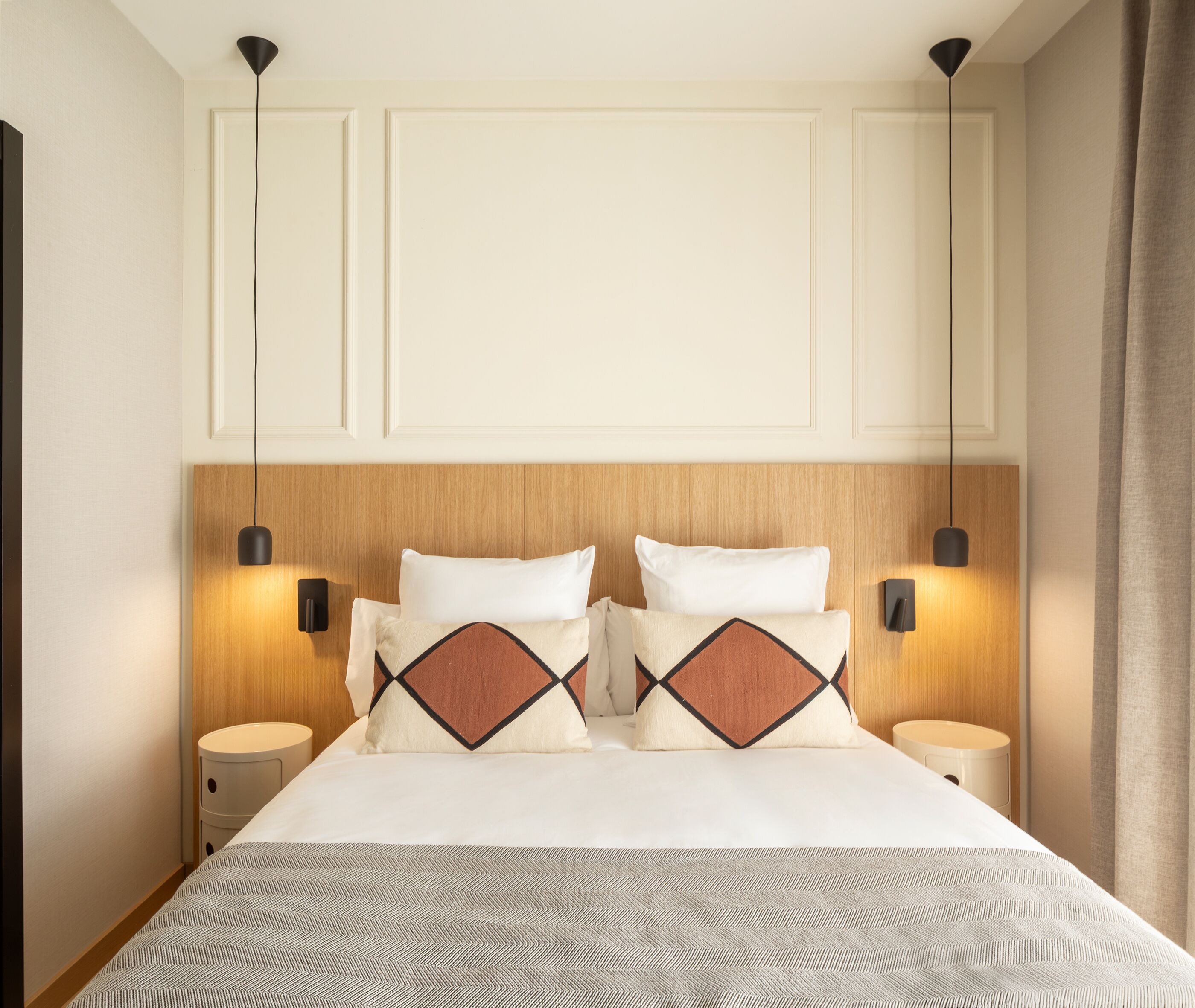 Une chambre d’hôtel avec un grand lit, deux tables de chevet, une tête de lit en bois et des lampes suspendues.
