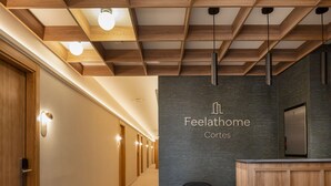 Un comptoir d’accueil avec une enseigne indiquant « Feelathome Cortes », un plafond en bois avec des poutres apparentes et un couloir recouvert de moquette.