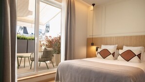 Une chambre avec une grande fenêtre, un lit agrémenté d’oreillers à motifs, une table de chevet et une chaise à l’extérieur.