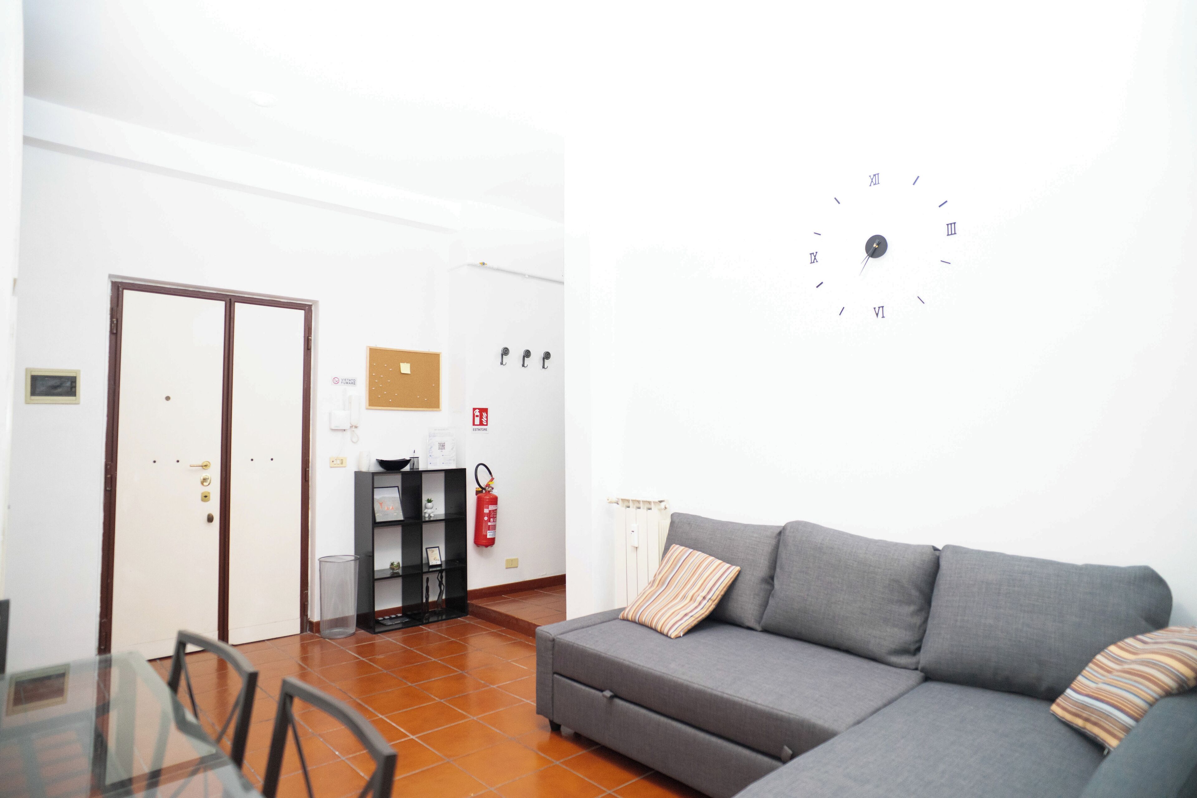 A modern living room with a grey sofa, a glass dining table, and a white wall clock.