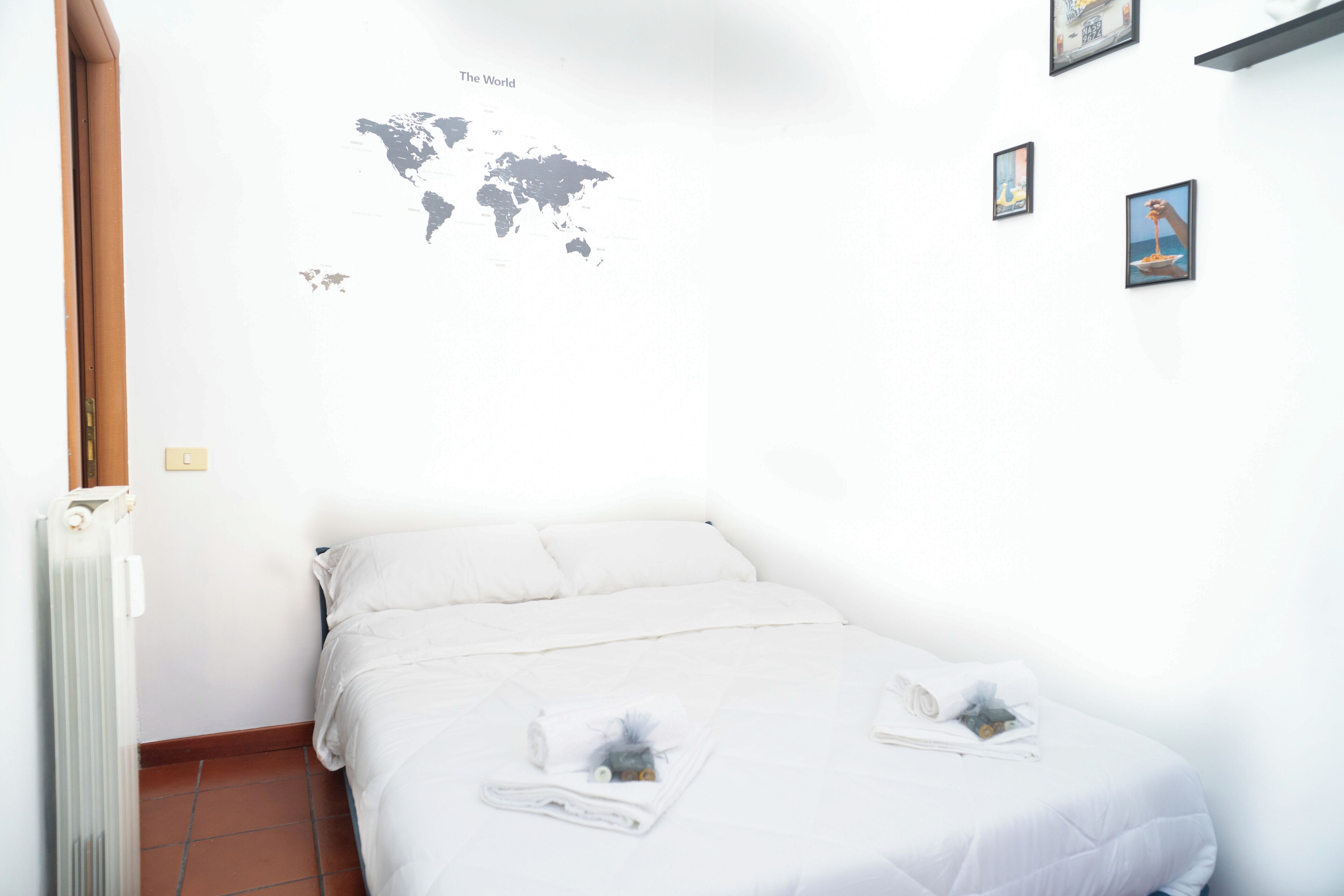 A neatly made bed with white linens and towels, a world map on the wall, and a small framed picture.