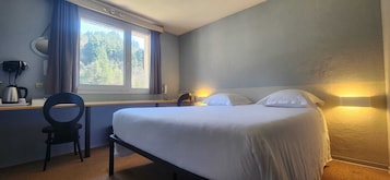 A bedroom with a bed, a desk with a chair, a window with curtains, and a wall-mounted lamp.