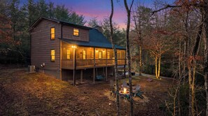 A wooden cabin with a deck, surrounded by trees.