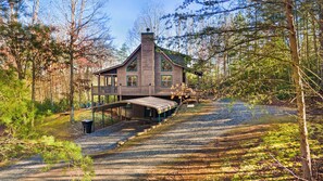A wooden cabin with a covered deck, surrounded by a forest.