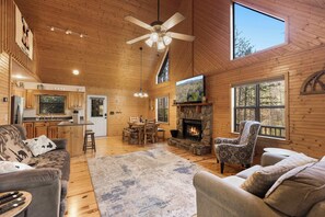 A spacious living area with a fireplace, wooden ceiling, and large windows.