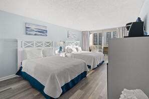 Habitación de hotel con dos camas, un escritorio, una silla, una ventana con cortinas y un balcón.