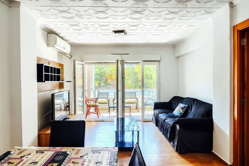 A living room with a sofa, a coffee table, a TV, and a sliding glass door leading to an outdoor area with chairs.
