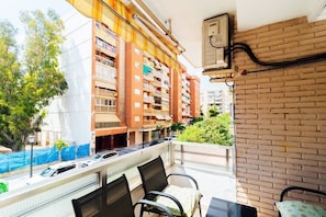 Un balcon donnant sur un immeuble à plusieurs étages, avec une table, des chaises et un mur en briques.