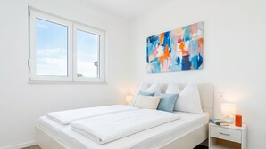 Un dormitorio con una cama, una mesita de noche, una obra de arte en la pared y una ventana.