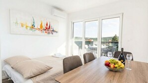 Una habitación con una cama, una mesa de comedor con frutas y vino, y vistas a la ciudad a través de grandes ventanales.