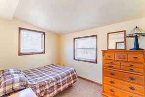 A bedroom with a bed, a dresser, two windows with blinds, and a ceiling fan.