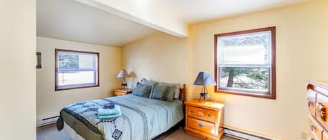 A bedroom with a bed, two bedside tables, a dresser, and two windows.