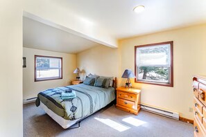 A bedroom with a bed, two bedside tables, a dresser, and two windows.