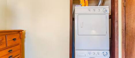 A compact, white stacked washer and dryer unit with a wooden cabinet to the left.