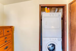 A compact, white stacked washer and dryer unit with a wooden cabinet to the left. - Cozy 3-bedroom cottage in Hunter, NY (Hunter)