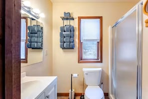 A bathroom with a toilet, sink, mirror, and a window with blinds.