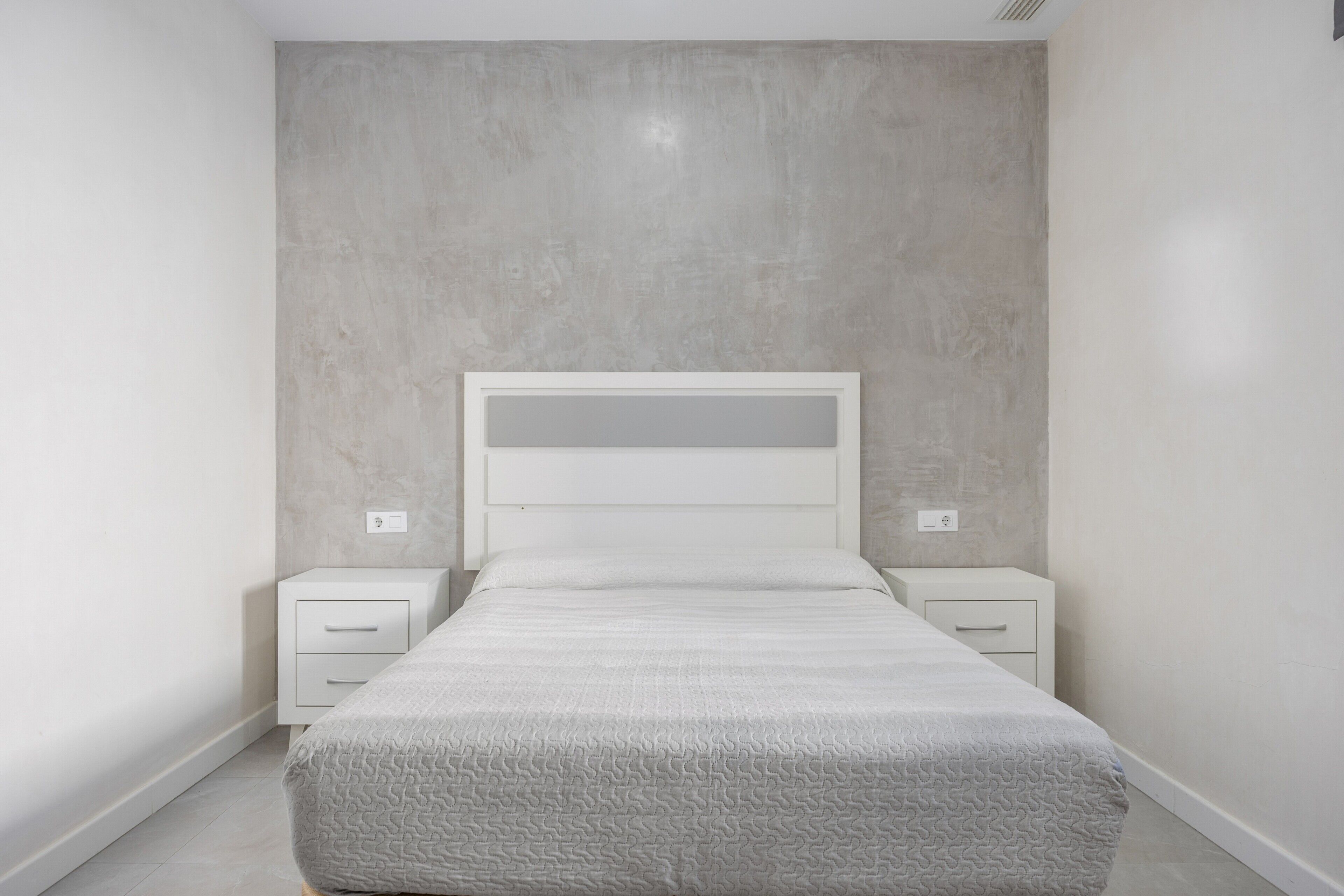 A bedroom with a bed, two bedside tables, and a plain wall.